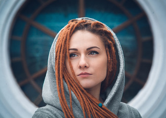 Portrait of a girl with dreadlocks of red color in a white sweatshirt with a hood on the background...