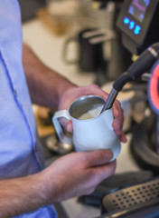 Fototapeta na wymiar Barista steaming milk on espresso machine in coffee shop