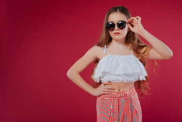 fashion concept - portrait of a beautiful little girl in big hat and sunglasses.Stylish girl in sunglasses, with long hair in shorts and a white top, on a summer vacation