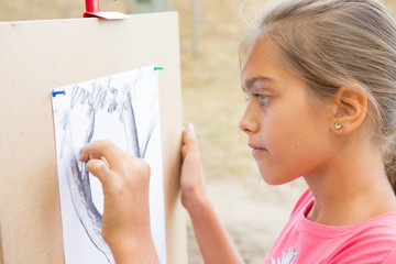 girl draws the lead. Summer creative activity for teenagers. Girls Hand draws a pencil tree trunk on a white sheet. A drawing of nature in black and white
