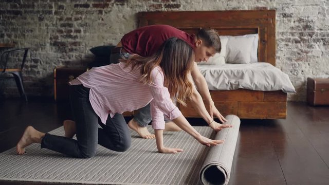 Happy husband and wife are unrolling carpet in their new house in bedroom then kissing enjoying beautiful bedroom. Renovation, relocation, stylish interior concept.