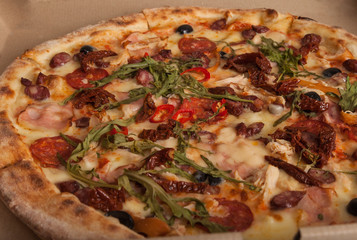 Delicious crispy Italian pizza on craft paper cardboard. Closeup of Pizza with salami, sausages, olives, hot red chili peppers, ham and sun-dried tomatoes. Restaurant menu, Italian food. Delivery