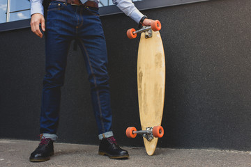 low section of stylish man standing on longboard on street
