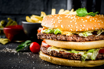 Various party food, Hamburgers, French fries, potato chips, pickled cucumbers, onions, tomatoes and cold beer bottles, rusty black concrete background copy space