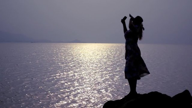 A lush girl in a hat and dress is standing on the beach on the lodges and making a selfie. slow motion, 1920x1080, full hd