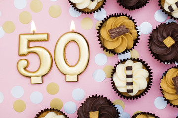 Number 50 gold candle with cupcakes against a pastel pink background