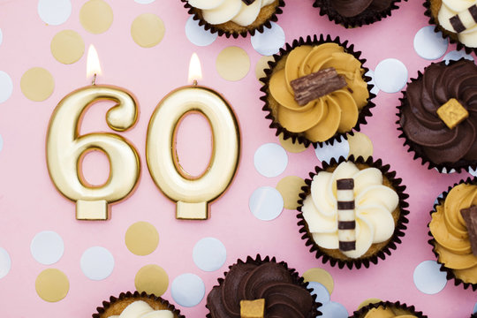 Number 60 gold candle with cupcakes against a pastel pink background