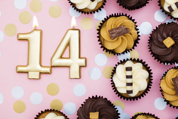 Number 14 gold candle with cupcakes against a pastel pink background