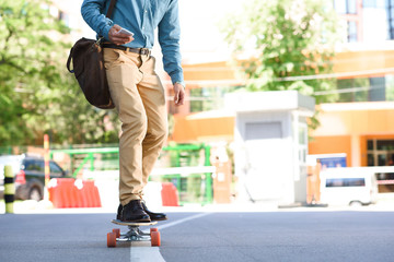 cropped shot of young man using smartphone and riding skateboard on street