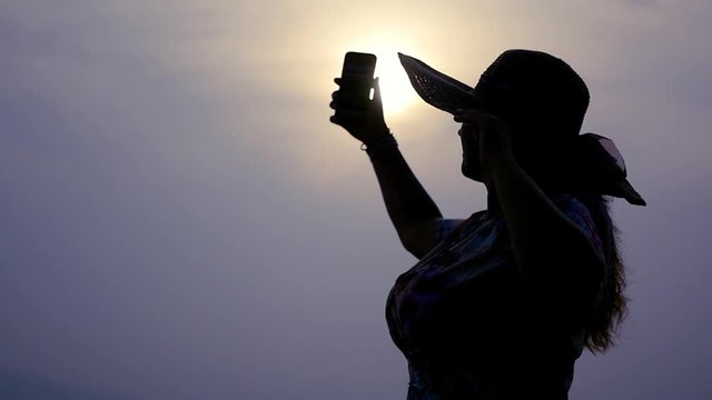 A girl with a lush breasts is standing on the beach at sunset, making a selfie in a hat. slow motion, 1920x1080, full hd