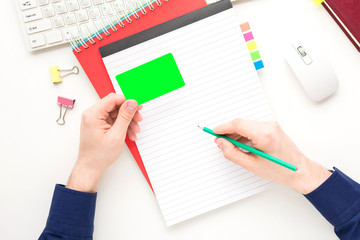 white Desktop, male hands, guy holding a business card, guy writes in a Notepad, notebook, white background with copy space, for advertisement, top view