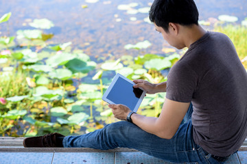 Backpackers or travelers are holding tablets while sitting near the river.