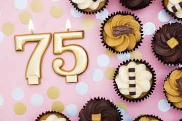 Number 75 gold candle with cupcakes against a pastel pink background
