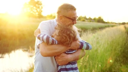 Elderly grandfather and loving grandson smiling and hugging each other outdoors, on the river bank. Two generations. Colorful sunset. A happy family - Powered by Adobe