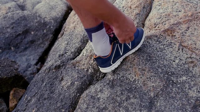 A man ties up his shoelaces on sneakers before training on rocks. slow motion, 1920x1080, full hd
