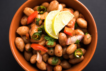 Boiled Peanut Chaat or Chatpata sing dana or shengdana or mungfali. served in a ceramic bowl over moody background