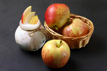 Food. Dessert of milk. Dairy product on a black background. Creamy yogurt in a glass jar with pieces of fresh juicy pears and red apples for a healthy diet.