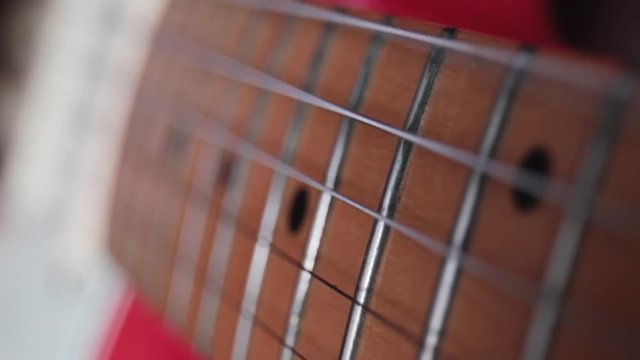 Strings of vibrating red electric guitar with detailed images of neck and scale. Vibration of the strings of the musical instrument in camera in super slow motion