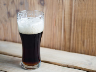 A glass of cold dark beer on a wooden table
