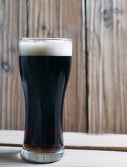 A glass of cold dark beer on a wooden table