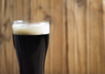 A glass of cold dark beer on a wooden table