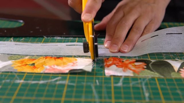 A tailor woman cuts the lining material on the cutting mat with a sewing knife.