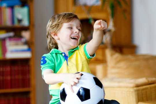 Little blond preschool kid boy with ball watching soccer football cup game on tv.