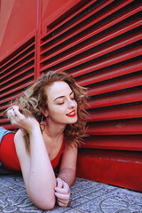 Plakat Atractiva mujer rubia vestida de rojo con un estilo urbano con una pared roja de fondo 