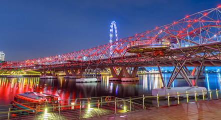 Fototapeta na wymiar Architecture of pedestrian bridge, ferris wheel in the background illuminated at dusk. Cruise docked at North Jetty Bayfront in Marina Bay Area, Singapore city. Famous place for travel destination.