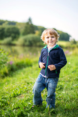 Little blond kid boy playing near forest lake on summer evening. cute child with curly hairs playing. Family on weekend or vacations