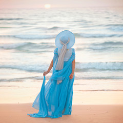 Anonymous slim girl in romantic dress and hat looking on the sun set or sunrise unbove the sea. Coastal vacation, 