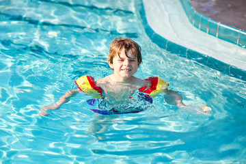 Happy little kid boy having fun in an swimming pool. Active happy preschool child learning to swim. with safe floaties