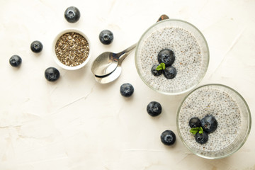 Two portions of chia pudding with vegan almond milk, blueberry & seeds on the side, served in glasses. Healthy vegetarian breakfast, berries & greek yogurt, spoon. Background, copy space, close up.