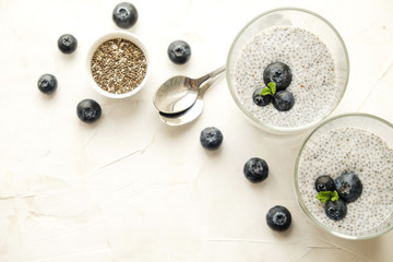 Two portions of chia pudding with vegan almond milk, blueberry & seeds on the side, served in glasses. Healthy vegetarian breakfast, berries & greek yogurt, spoon. Background, copy space, close up.