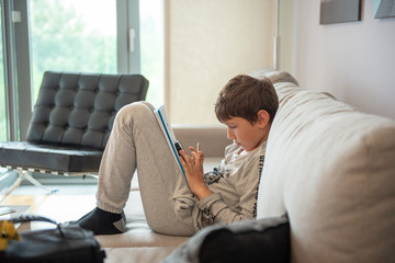 Young boy sitting in living room, looking to smartphone and drawing