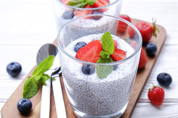 Two portions of chia pudding with vegan almond milk, blueberry & strawberry, mint, served in glasses. Healthy vegetarian breakfast, seeds, berries, greek yogurt, spoon. Background, close up, top view.