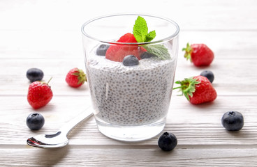 Portion of chia pudding with vegan almond milk, blueberry & strawberry, mint, served in glass. Healthy vegetarian breakfast, seeds, berries, greek yogurt, wooden table. Background, close up, top view.