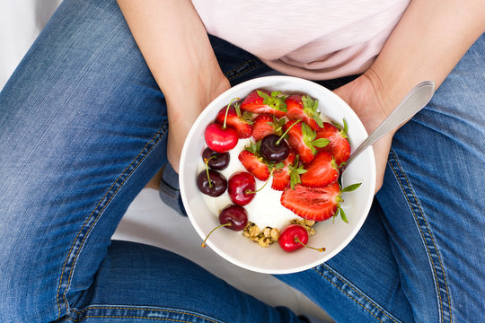 Healthy eating concept. Women's hands holding bowl with muesli, yogurt, strawberry and cherry. Top view. Lifestyle
