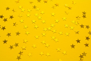 Golden star shaped confetti on yellow paper background. Top view