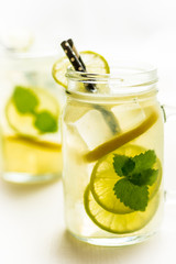 Lemonade Mojito Cocktail with Cold Fresh Ice, Lemon and Mint Leaves in Mason Jar on White Wooden Background. Bright Summer Concept.