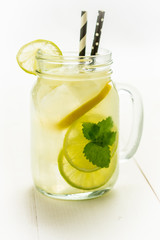 Lemonade Mojito Cocktail with Cold Fresh Ice, Lemon and Mint Leaves in Mason Jar on White Wooden Background. Bright Summer Concept.