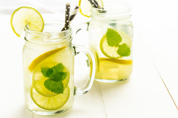 Lemonade Mojito Cocktail with Cold Fresh Ice, Lemon and Mint Leaves in Mason Jar on White Wooden Background. Bright Summer Concept.