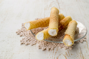 
  Sweet dessert. Wafer tubules with a delicate protein cream on a transparent round plate on an old wooden table. 