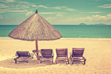 Straw beach umbrella and wooden reclining chairs on a perfect beach, vintage process