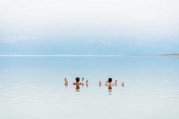 Young couple floating on surface of Dead Sea water and enjoying summer sun and vacation. Recreation...