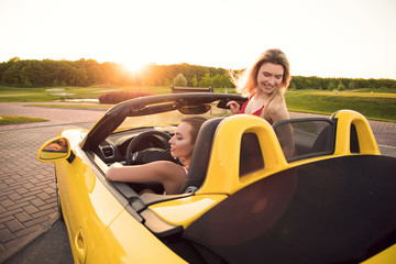 Female friendship! Two beautiful smiling best friends in the yellow cabriolet having a great...