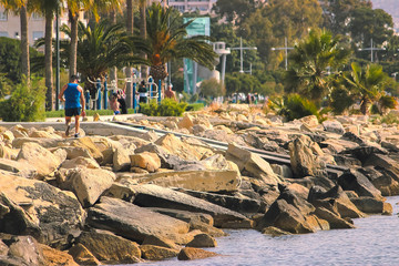 Middle age man at workout outdoors jogging along the sea at sunny day, at rocks
