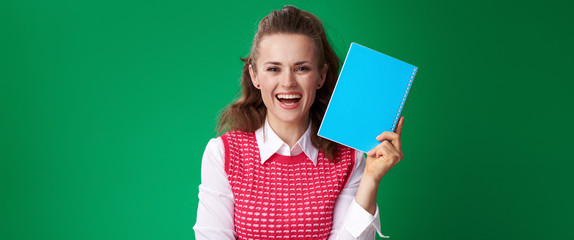 happy student woman showing blue notebook isolated on green