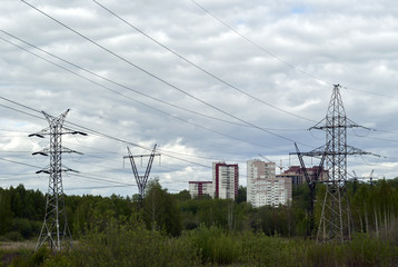 landscape - overgrown with bush terrain with numerous supports of transmission lines of various designs, with wires leading to residential areas on the horizon