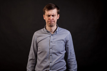 Obraz premium A dark haired white man with a sad and boring face closed eyes in a plaid shirt and jeans on a black isolated background